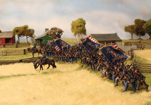 A photo of fully painted miniature figures and terrain for wargaming: a Union American Civil War army charging through a farm behind mounted officers