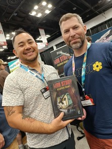 A photo of game illustrator Kwanchai Moriya and co-designer David Thompson holding a final box of War Story: Occupied France