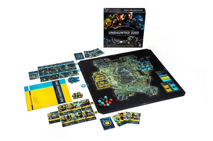A photo of a Callisto game board set up in front of the box with various dice, tokens, rulebooks and two player areas of cards