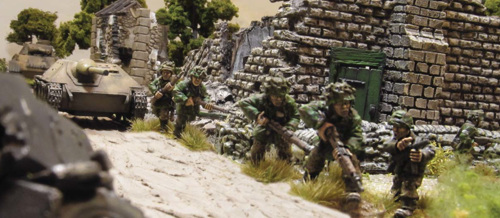 A photo of fully painted miniature figures and terrain for wargaming, showing an advance squad of WW2 German scouts going ahead of a tank column