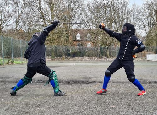 Two people leaning how to swordfight and wearing protective gear
