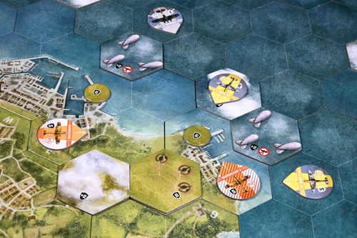A photo of example gameplay on the Undaunted: Battle of Britain board, made up of hex tiles depicting the British coastline, with various counters and tokens representing planes, barrage balloons, clouds and anti-aircraft guns