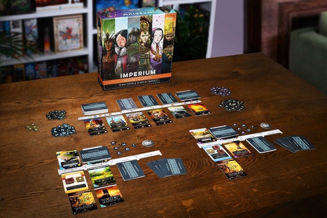 A photo of a fully set-up game of Imperium: Horizons on a table with the game box stood behind it and shelves full of board games in the background