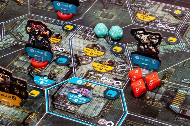 A close-up photo of a set-up game of Callisto showing an illustrated sci-fi map board divided into various different spaces, covered with various dice, cardboard tokens, unit counters and mech standees