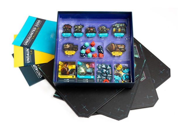 A photo of an opened Callisto box showing the insert with spaces for lal the components, on top of a spread of the game's various rulebooks and boards