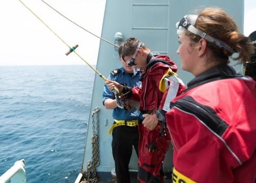 Royal Canadian divers in red dive suits are pulled from the water as part of an emergency training drill