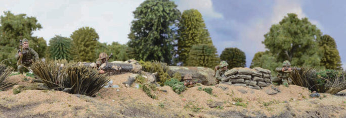 A photo of fully painted miniature figures and terrain for wargaming, depicting WW2 soldiers taking cover behind a ridge