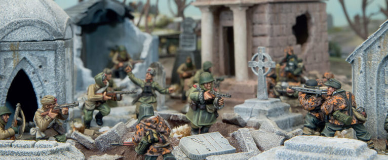 A photo of fully painted miniature figures and terrain for wargaming: WW2 soldiers fighting through a cemetery