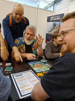 A photo of co-designer Trevor Benjamin explaining General Orders: World War II at SPIEL 2023